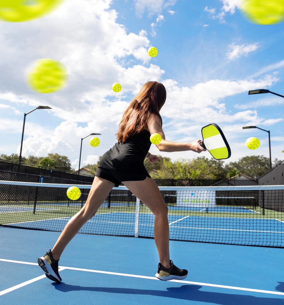 Pickleball player on court surrounded by flying pickleballs.