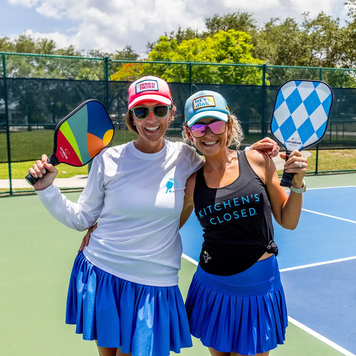 Two women on a pickleball court holding colorful paddles by Swinton