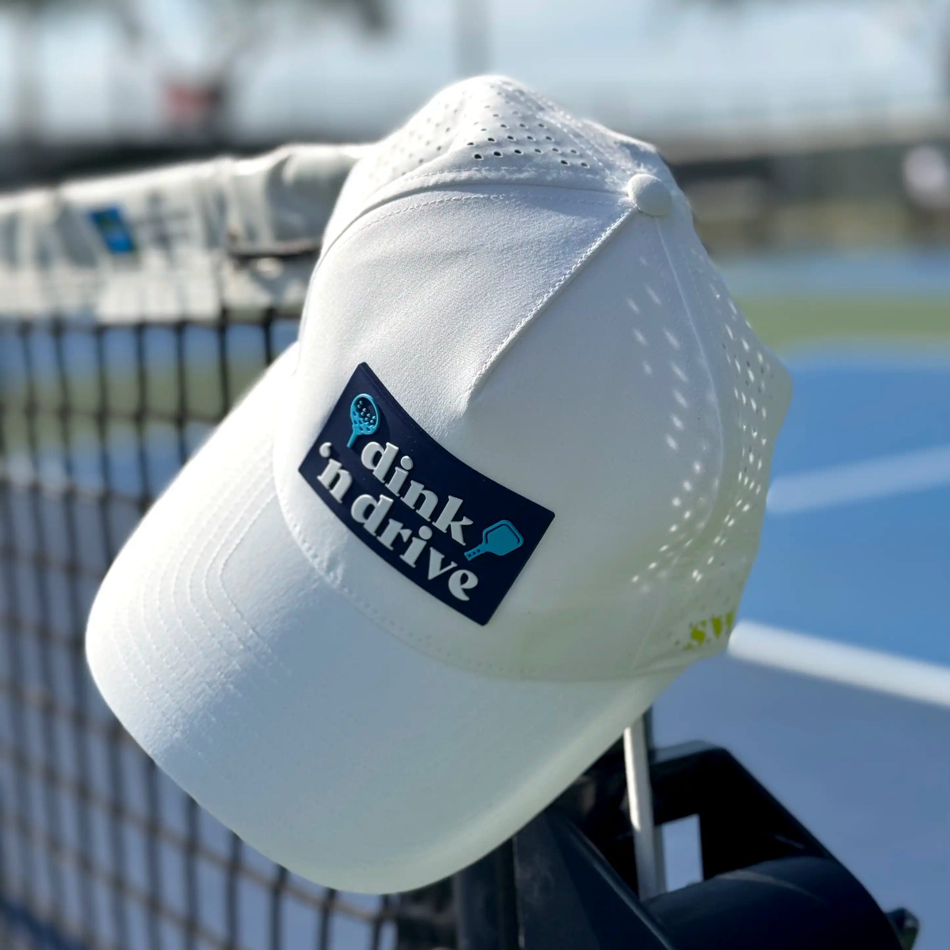 white pickleball hat hanging on net of pickleball court with golf and pickleball logo on front