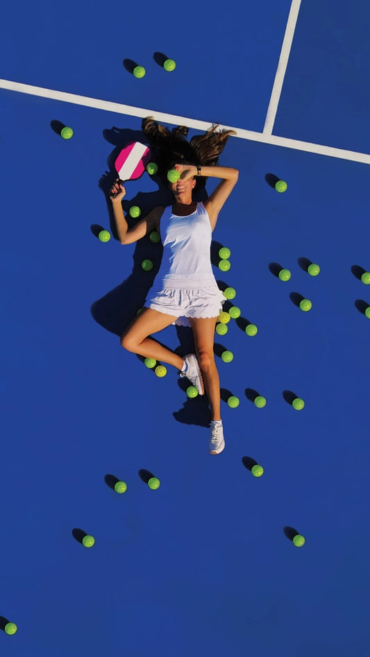 Pickleball player laying on court surrounded by pickleballs.