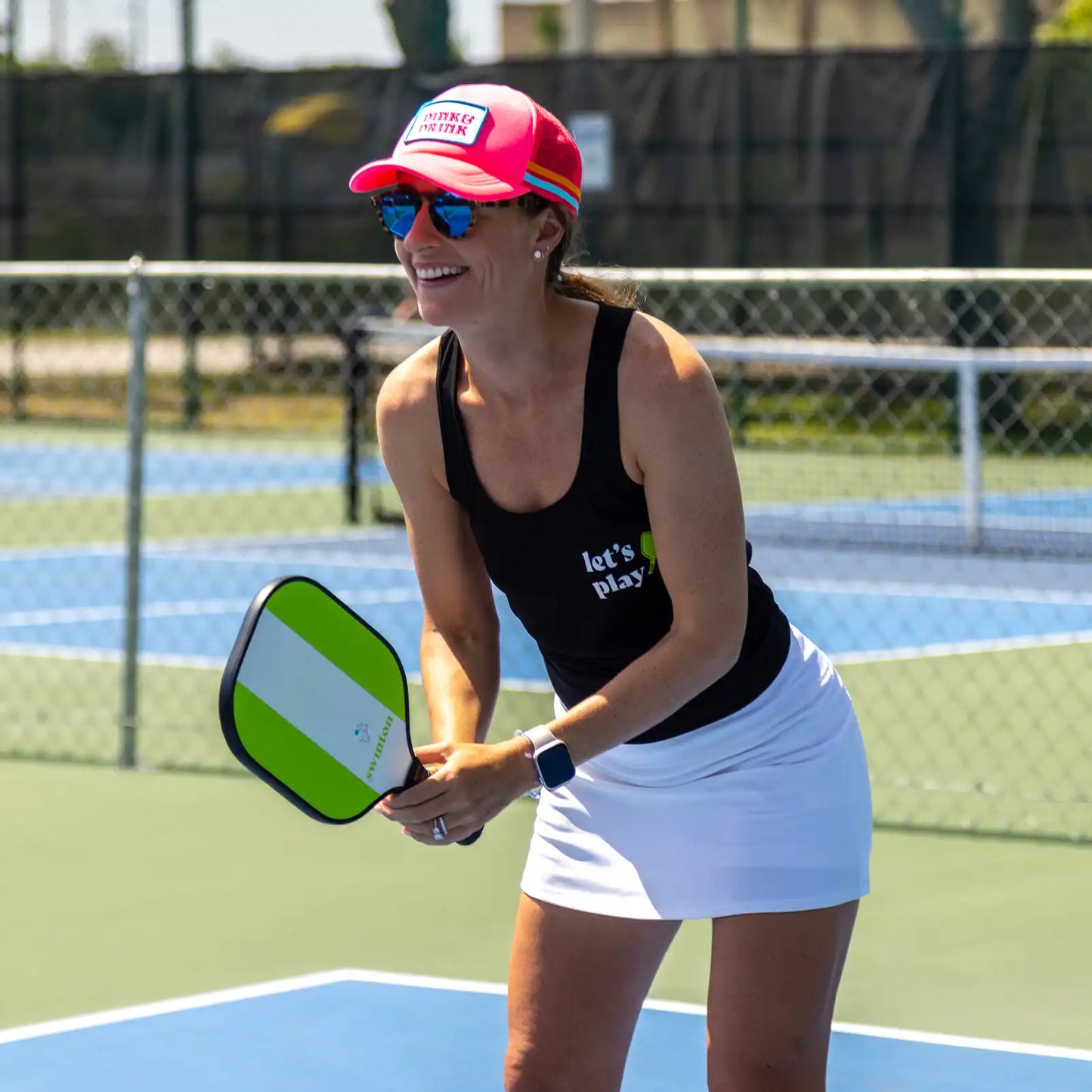 girl in pickleball ready position holding swinton paddle wearing pink hat and black let's play women's shirt