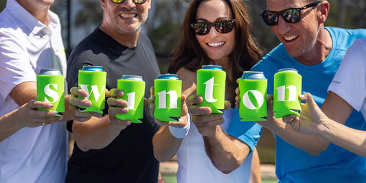 Pickleball players holding cans with koozies reading "swinton."
