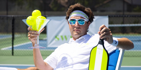 Pickleball player relaxing with giant martini glass filled with pickleballs.