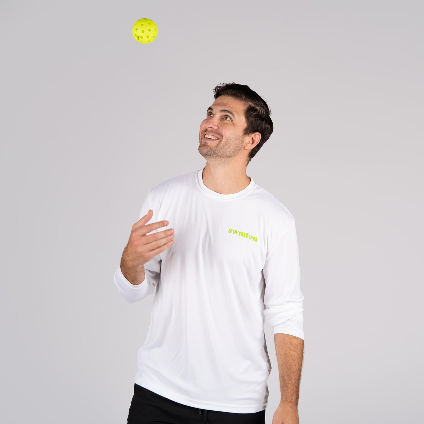 man wearing stay outta the kitchen long sleeve shirt throwing swinton pickleball into the air